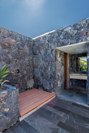 A stone-walled outdoor area with a wooden deck and a stone pathway leading to a door. - Casa Amazcala by Cosmos Homes (Zibatá)
