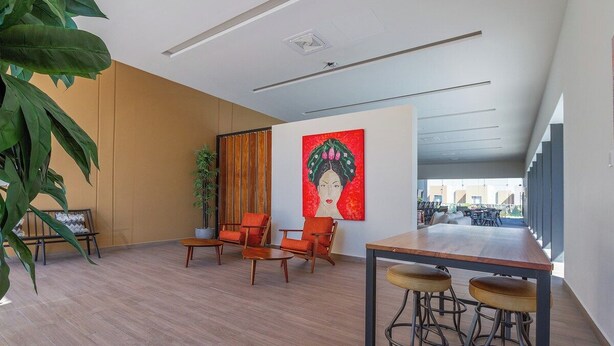 Un intérieur moderne avec un plancher en bois, un coin salon avec des fauteuils orange, un bar avec des tabourets et un grand tableau accroché au mur.