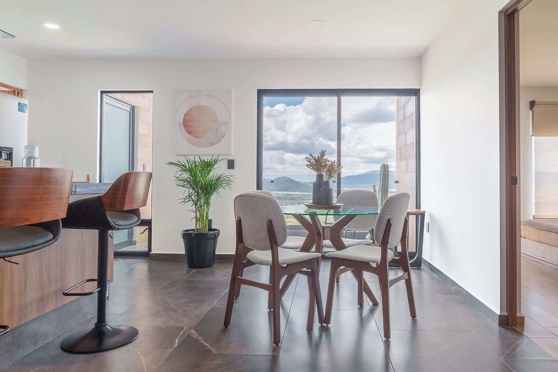 Ein moderner Essbereich mit einem Glastisch, Holzstühlen, einem Blumentopf und Blick ins Freie.