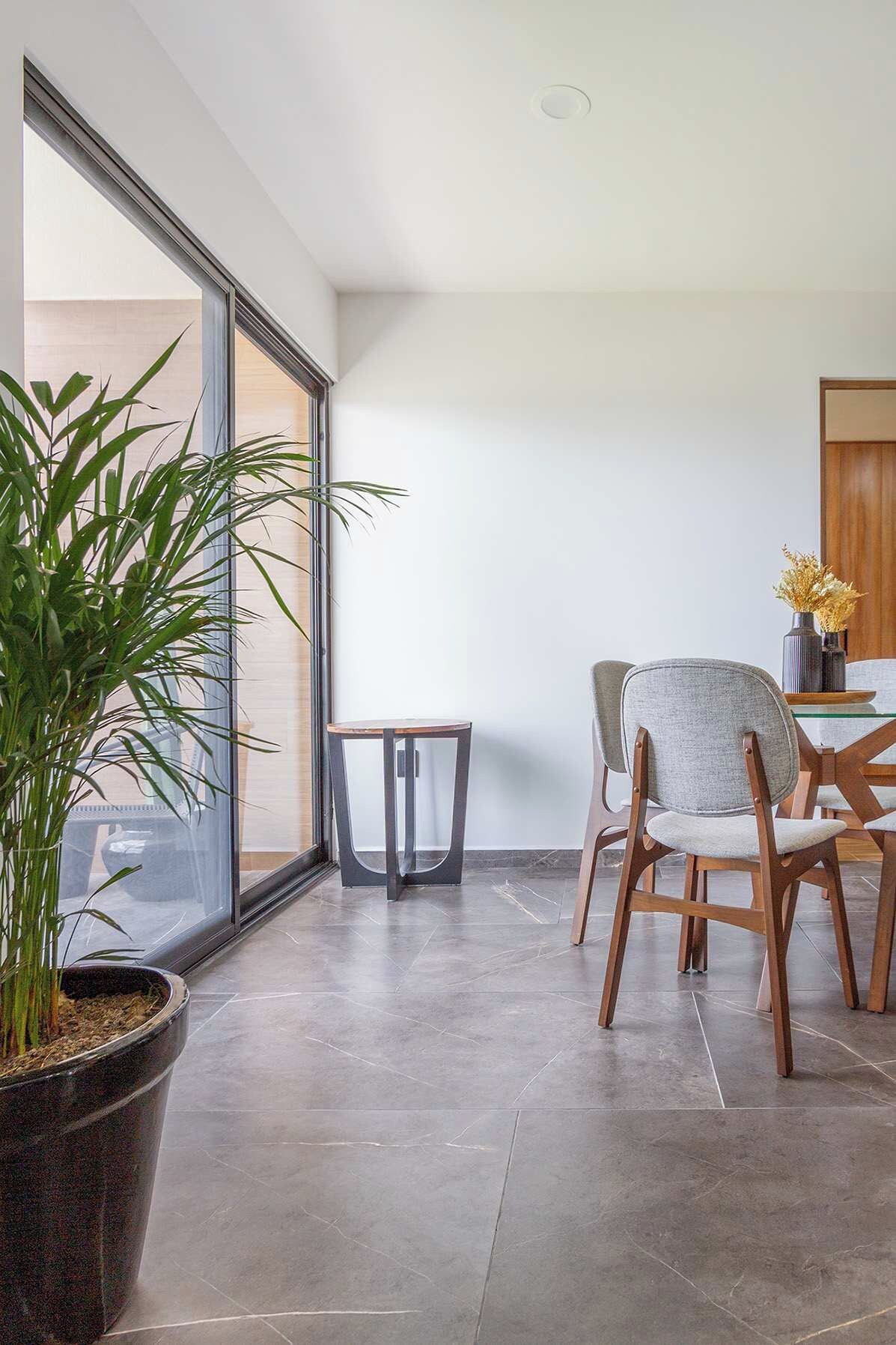 A modern dining area with a large window, a potted plant, and a table with chairs.