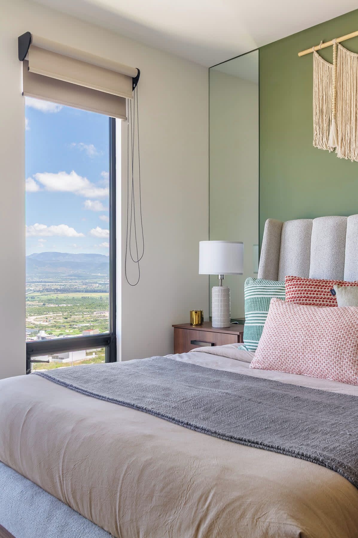 A hotel room with a large bed, a bedside table with a lamp, a mirror, and a view of the landscape.