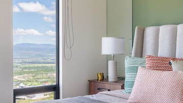 A hotel room with a large bed, a bedside table with a lamp, a mirror, and a view of the landscape.