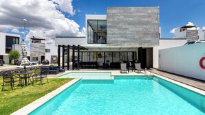 Un hotel moderno con piscina, area salotto all'aperto e cielo azzurro.