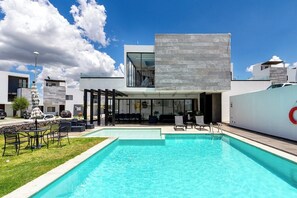 Een modern hotel met een zwembad, terras en helderblauwe lucht.