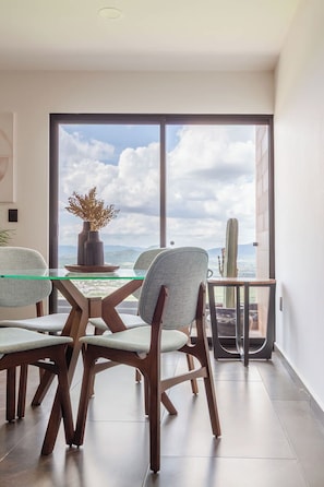Un espace repas moderne avec une table en verre, des chaises en bois et une vue sur le ciel et les montagnes.