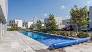 A swimming pool with a blue tarp on one side, surrounded by modern buildings and parked cars. - Casa Lele by Cosmos Homes (Zakia)