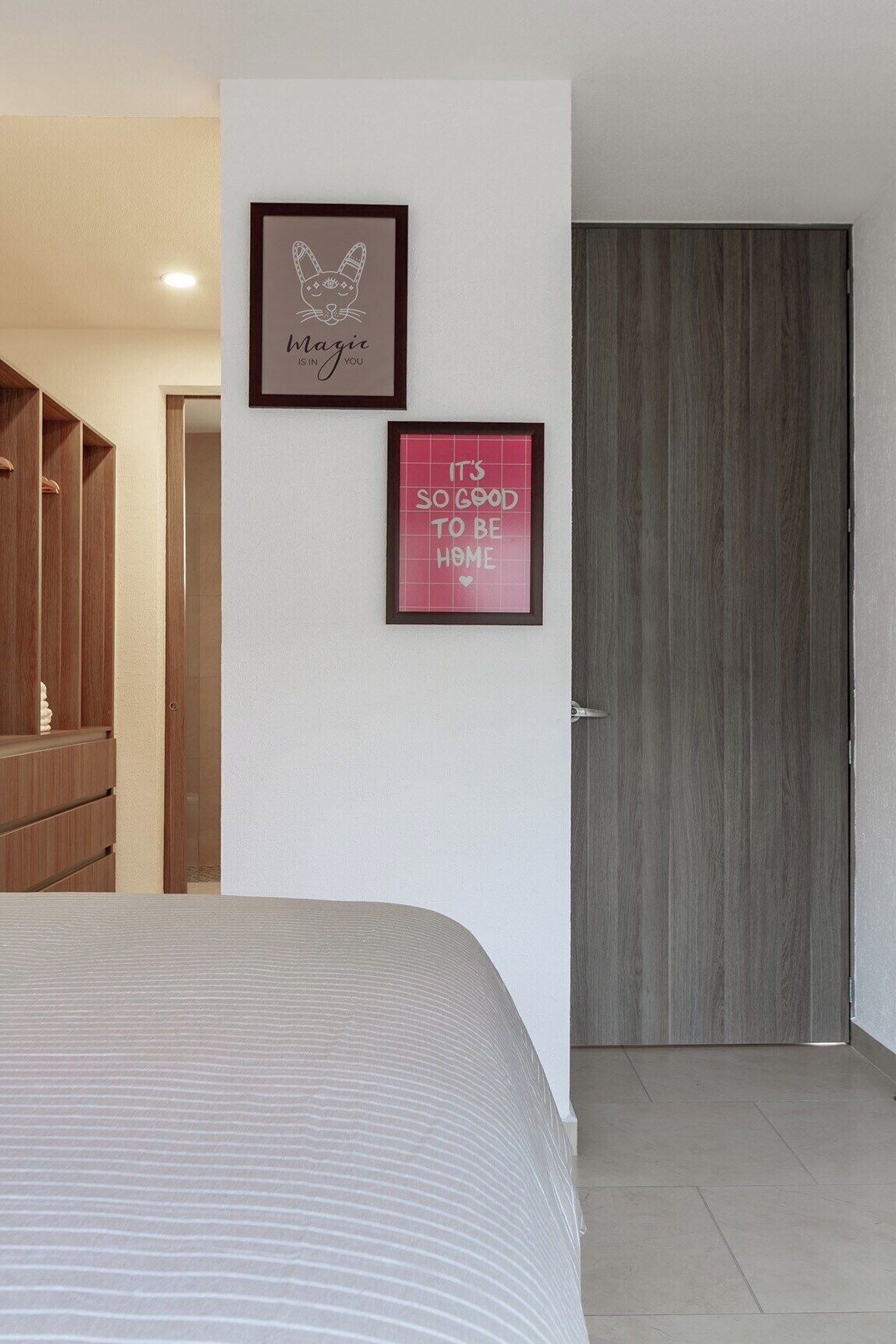 Quarto com cama, guarda-roupa e dois cartazes motivacionais emoldurados na parede.