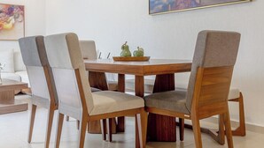 A dining area with a wooden table and four chairs, a painting on the wall, and a tiled floor. - Casa Lele by Cosmos Homes (Zakia)