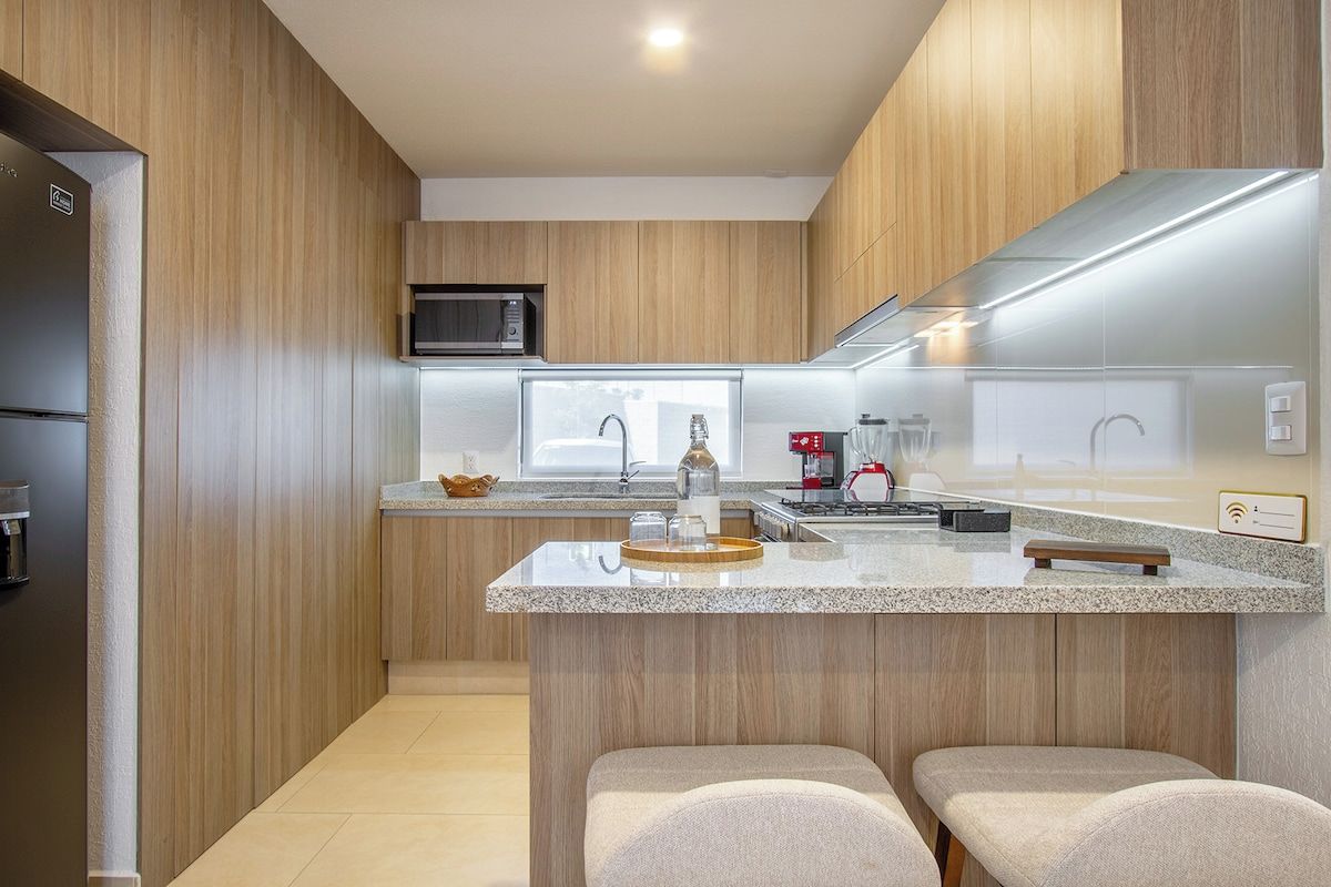 Cozinha moderna com painéis de madeira, ilha central com assentos, micro-ondas e máquina de café.