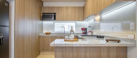 Une cuisine moderne avec un lambris en bois, un îlot central doté de sièges, un four à micro-ondes et une machine à café.