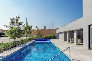 Una piscina con cubierta azul, rodeada de vegetación y un edificio moderno de techo plano.