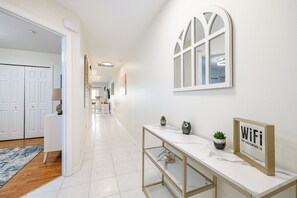 Een gang met een witte deur, een witte console tafel met een ‘WiFi’-bordje en een raam met een decoratieve lijst.