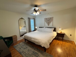 Une chambre à coucher comprenant un lit, un ventilateur de plafond, une lampe de chevet, un miroir mural et une décoration murale en macramé.