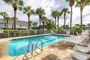 A swimming pool with a white fence, lounge chairs, and palm trees. - Welcoming 2-bedroom condo steps to Indian Rocks Beach (Indian Rocks Beach)