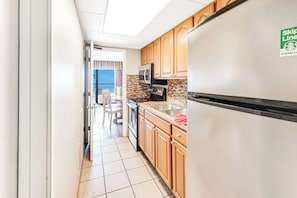 A narrow kitchen with wooden cabinets, a stainless steel refrigerator, and a microwave. - Amazing Oceanfront View  Condo with Pool & Hot tub (Myrtle Beach)