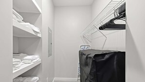 Una cabina armadio stretta con scaffali bianchi, un'asta di asciugatura in metallo e un oggetto coperto sulla destra.