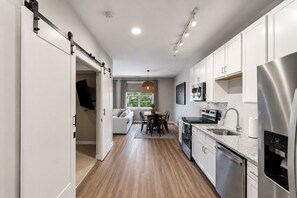 A modern kitchen with white cabinets, stainless steel appliances, and a wooden floor.