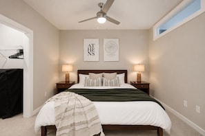 A bedroom with a bed, two bedside lamps, a ceiling fan, and two wall art pieces.