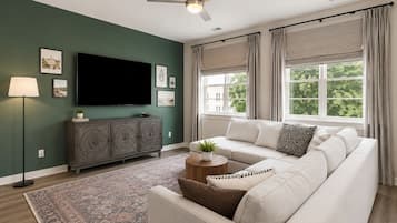 A living room with a sofa, a television, a cabinet, a floor lamp, and a window with curtains.