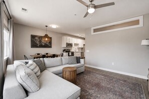 A modern living room with a sectional sofa, a dining table, and a kitchen in the background.