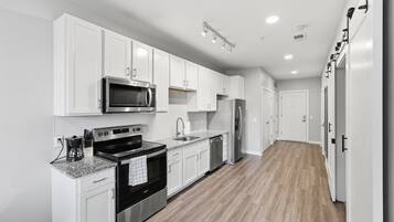 A modern kitchen with white cabinetry, stainless steel appliances, and a wooden floor.
