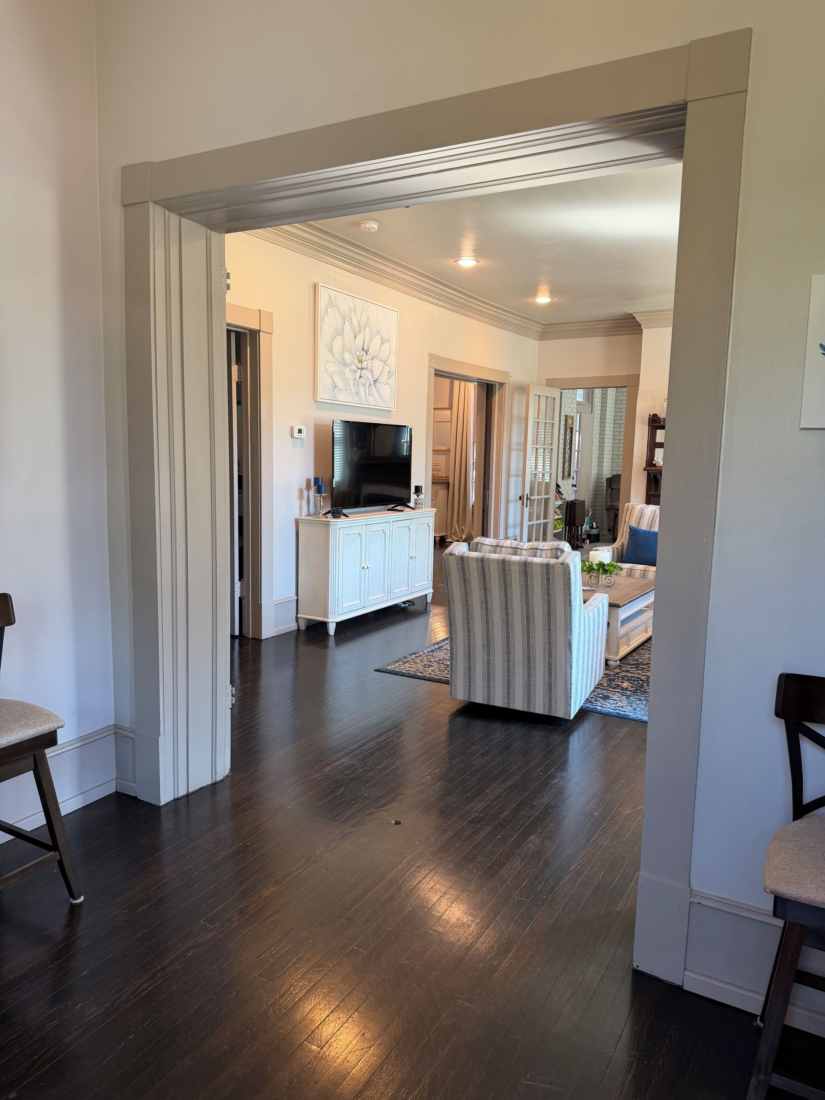 A spacious living area with a dark wooden floor, a white entertainment unit, and a striped sofa.