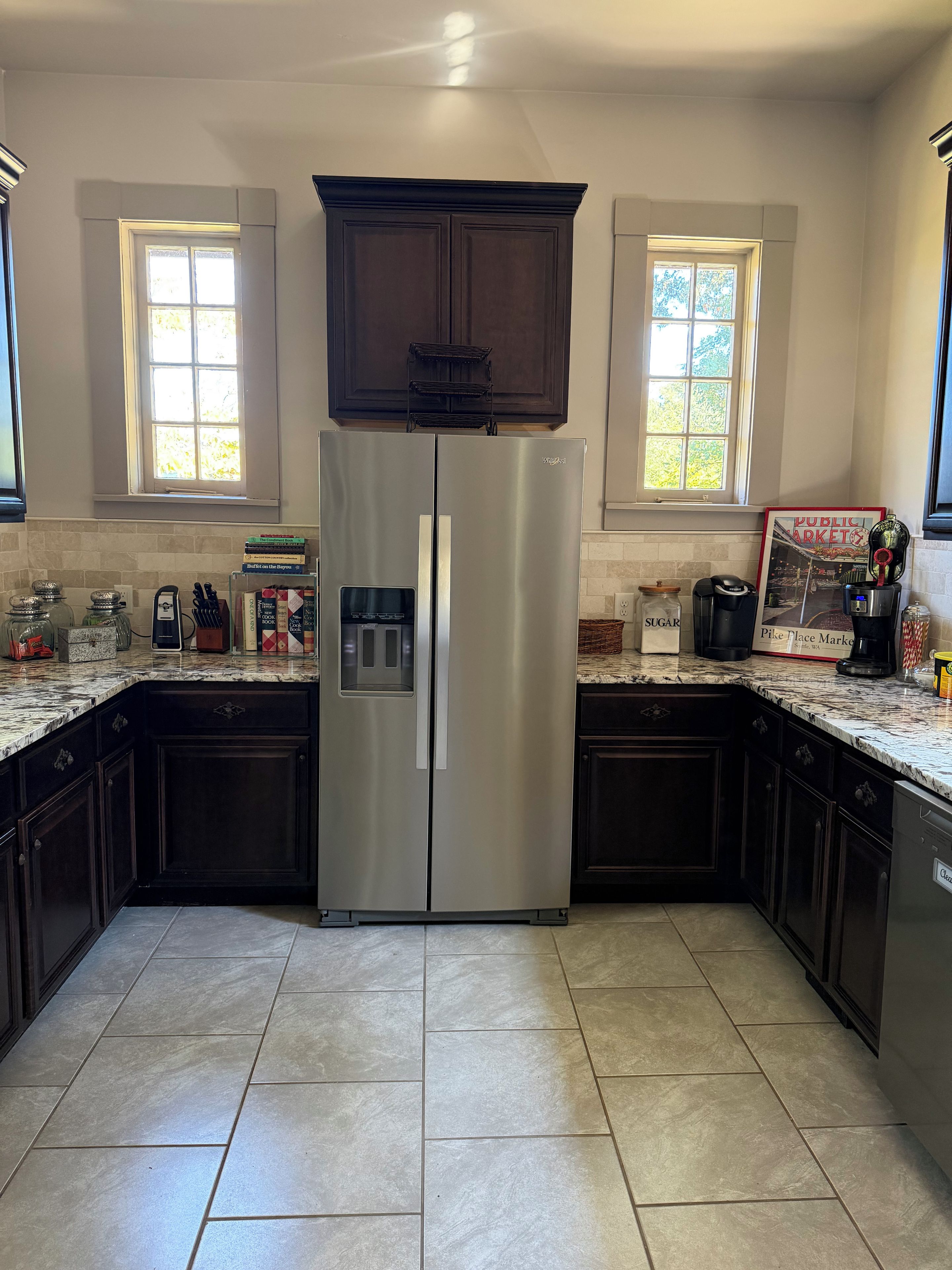 A kitchen with a stainless steel refrigerator, dark wooden cabinets, and a tiled floor.