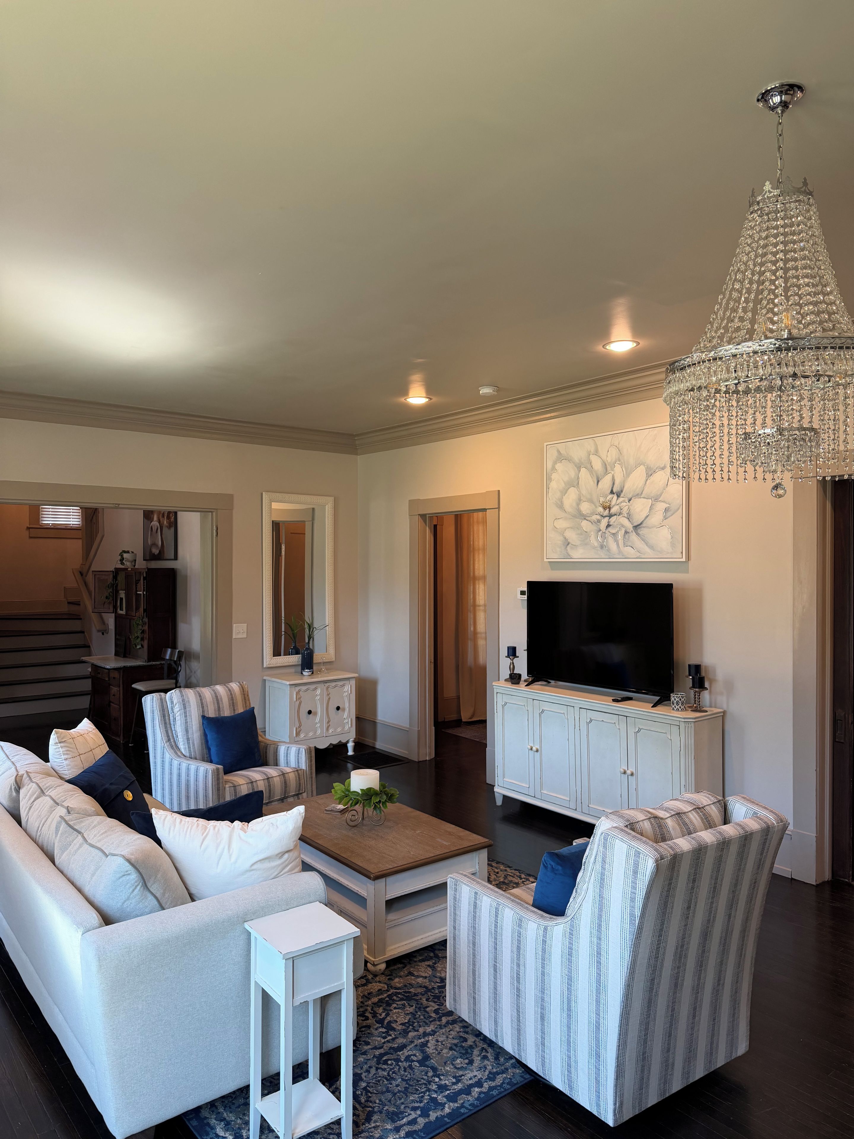 A living room with a sofa, armchair, TV, and chandelier.