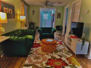 A living room with a green sofa, a tufted ottoman, a television, and a floral rug.