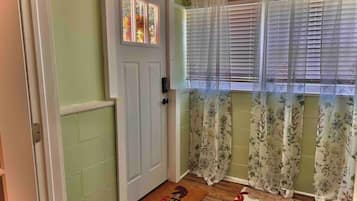 A hallway with a door, a window with blinds, and a floral curtain.