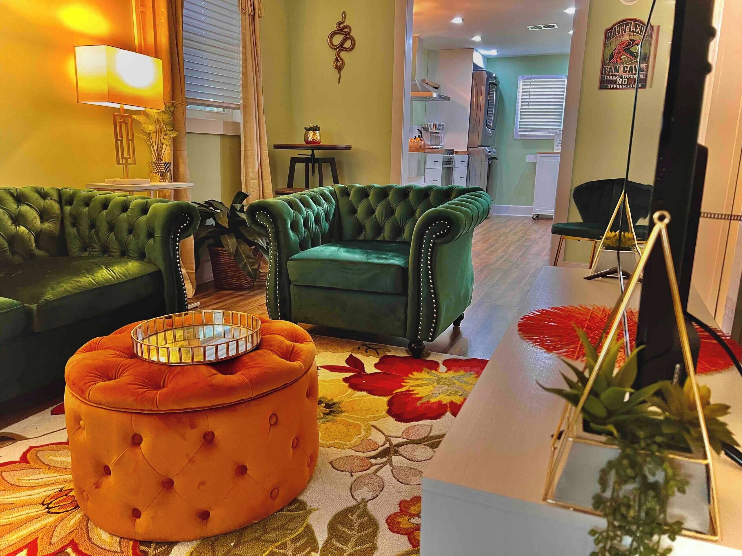 A living room with a green sofa, an orange ottoman, and a patterned rug.