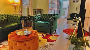 A living room with a green sofa, an orange ottoman, and a patterned rug.