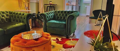 A living room with a green sofa, an orange ottoman, and a patterned rug.