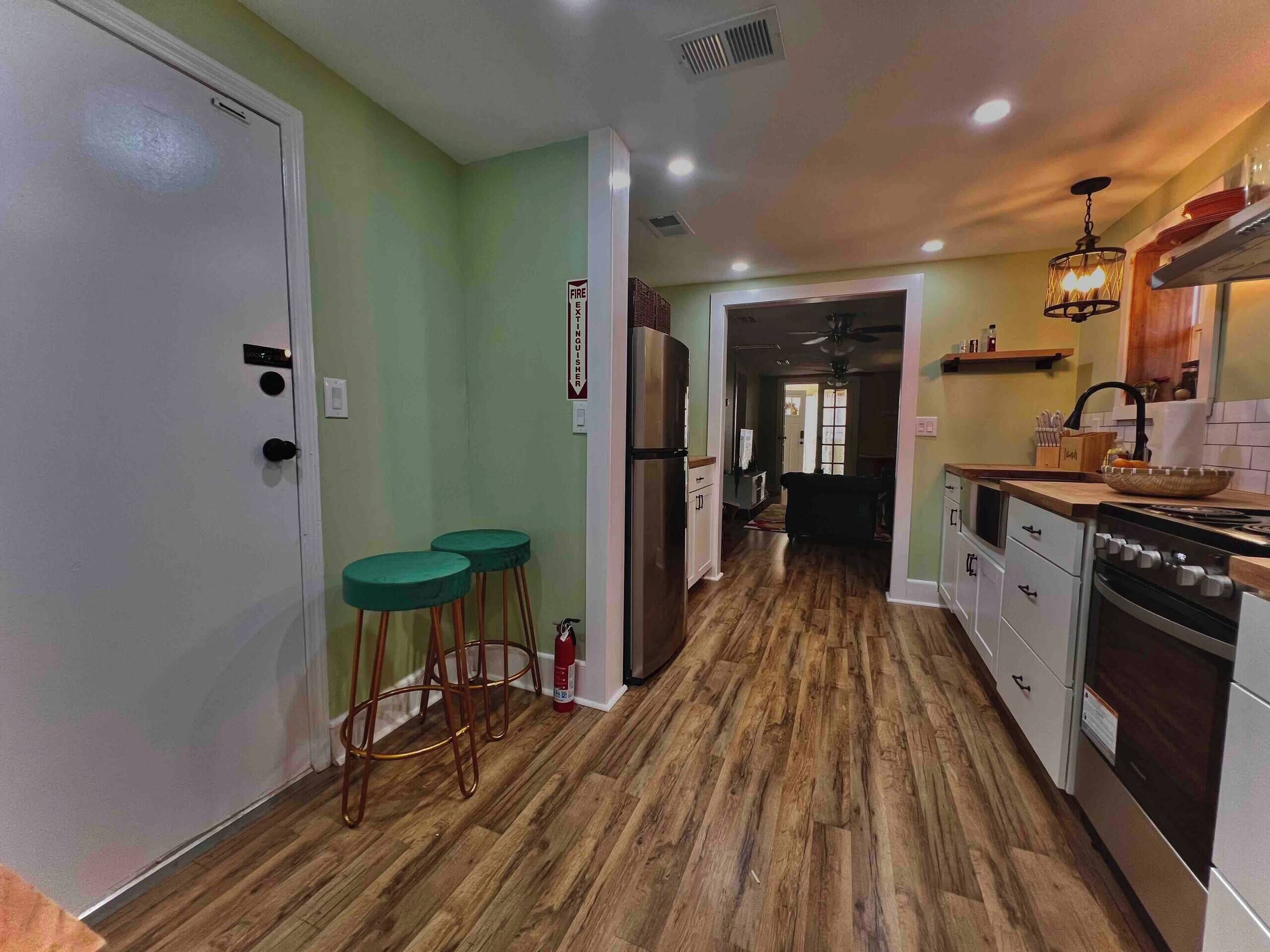 Una cocina con piso de madera, un refrigerador, una estufa y un comedor con taburetes.