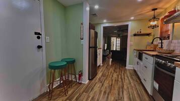 A kitchen with wooden flooring, a refrigerator, a stove, and a dining area with stools.