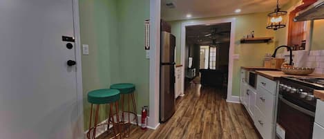 Una cocina con piso de madera, un refrigerador, una estufa y un comedor con taburetes.