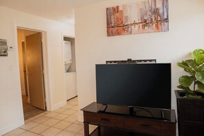 A room with a flat-screen TV on a wooden stand, a painting on the wall, and a potted plant. - Newly Renovated Spacious Stay Near Casino, Boston, Cambridge, & Somerville (Everett)