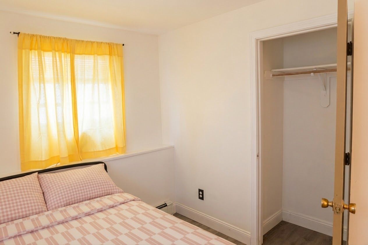 A bedroom with a bed, a window with yellow curtains, and a closet with a door.