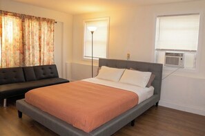 A bedroom with a bed, a sofa, a standing lamp, and an air conditioning unit. - Newly Renovated Spacious Stay Near Casino, Boston, Cambridge, & Somerville (Everett)