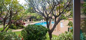 A pool area with a covered seating area, surrounded by lush greenery and a building in the background. - Haleakala Shores | 4BR Total | Sleeps 12 (Kihei)