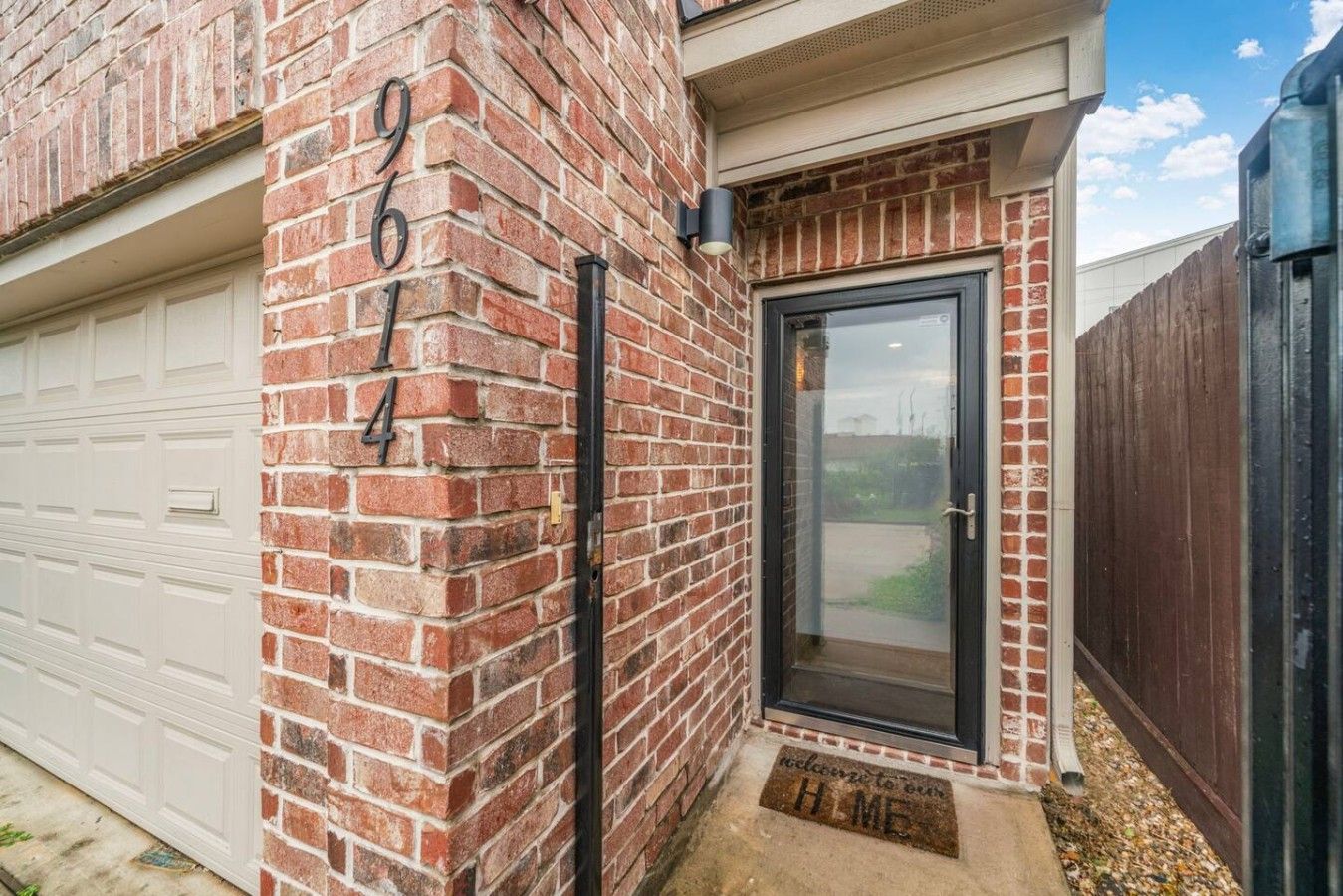 Een bakstenen huis met een garage, een zwarte deur en een voetmat.