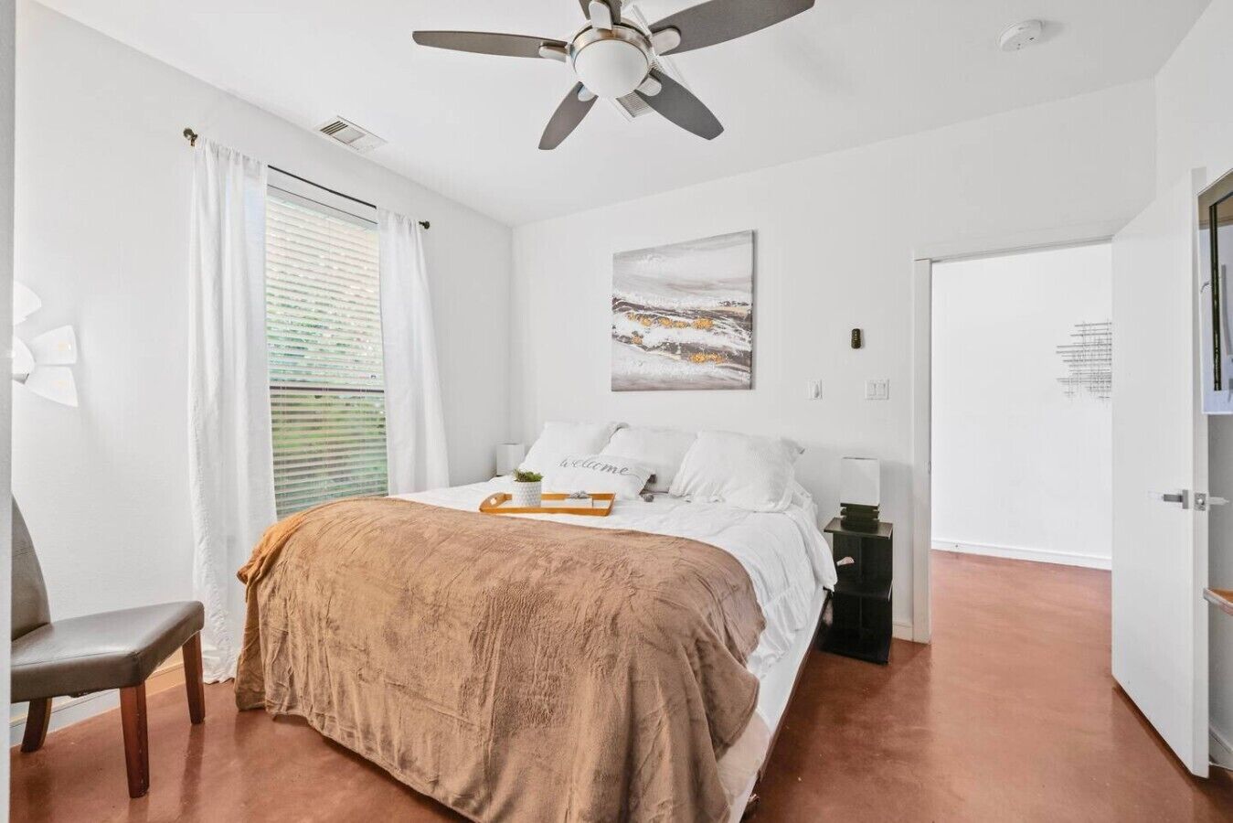 A bedroom with a bed, a bedside table, a ceiling fan, a window with curtains, and a door.
