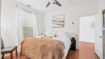A bedroom with a bed, a bedside table, a ceiling fan, a window with curtains, and a door.