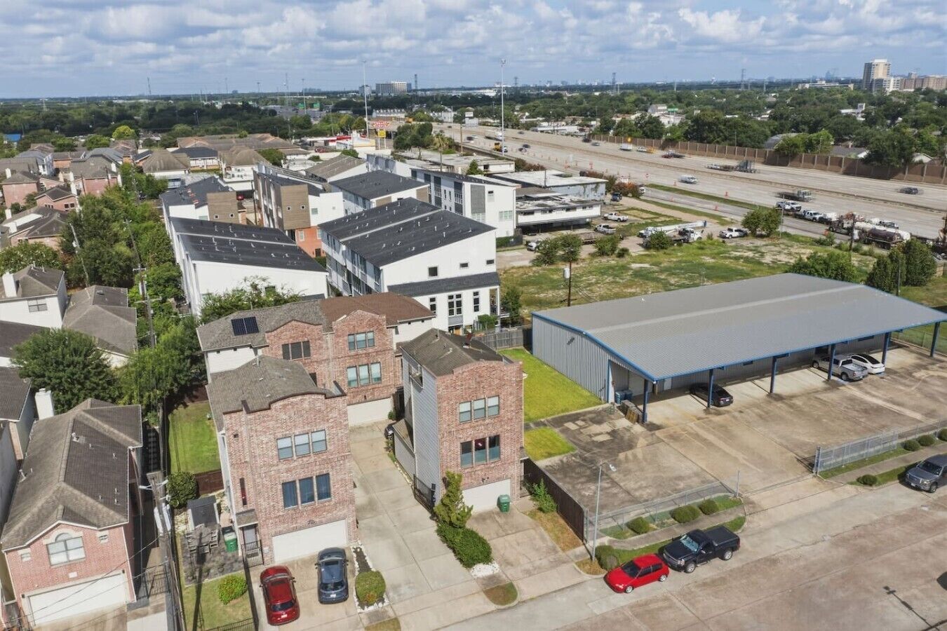 Un quartier résidentiel avec des maisons, un grand bâtiment industriel et une autoroute en arrière-plan.