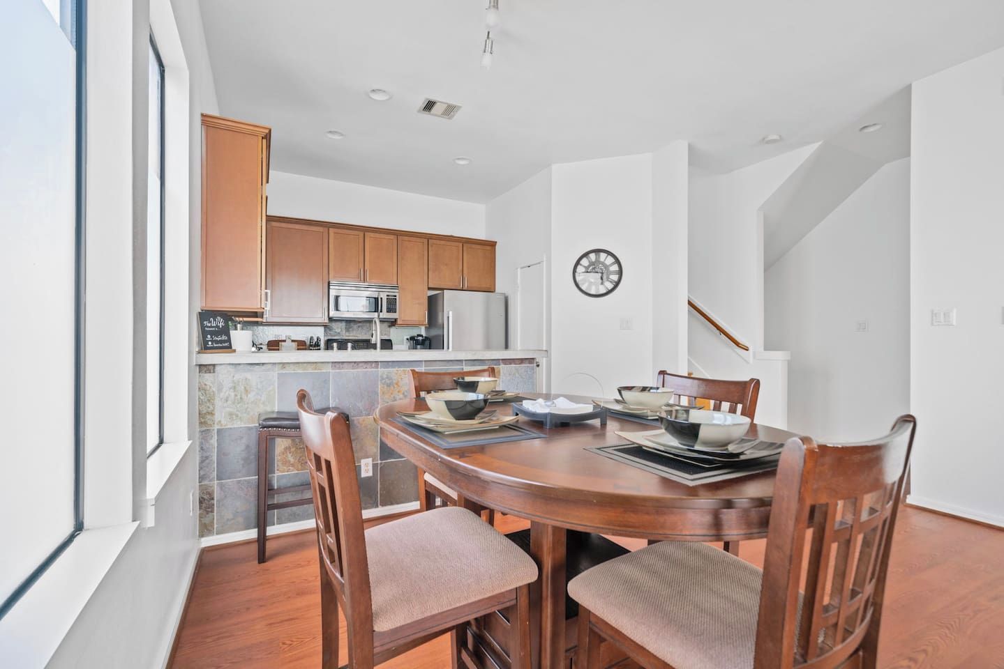 Une cuisine moderne avec des meubles en bois, une table à manger avec des chaises et une horloge au mur.