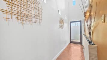 A corridor with a modern design, featuring a wooden art installation on the left wall and a vase with branches on the right.