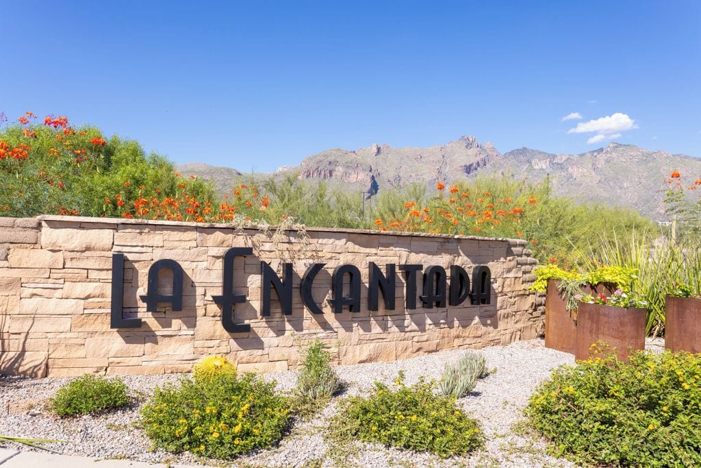 A stone wall with the text 'LA ENCANTADA' and a mountainous backdrop.