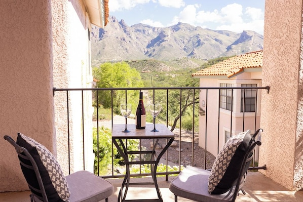 A balcony with two chairs, a table, and a bottle of wine.