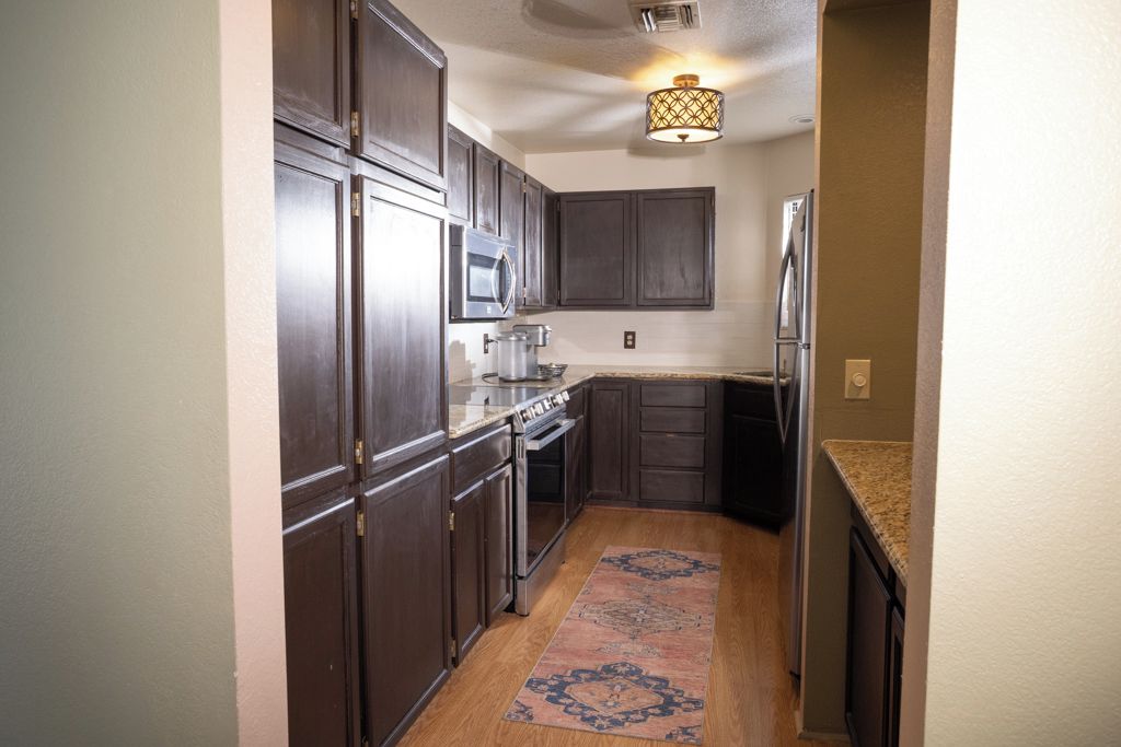 A kitchen with dark wooden cabinets, stainless steel appliances, and a patterned rug.