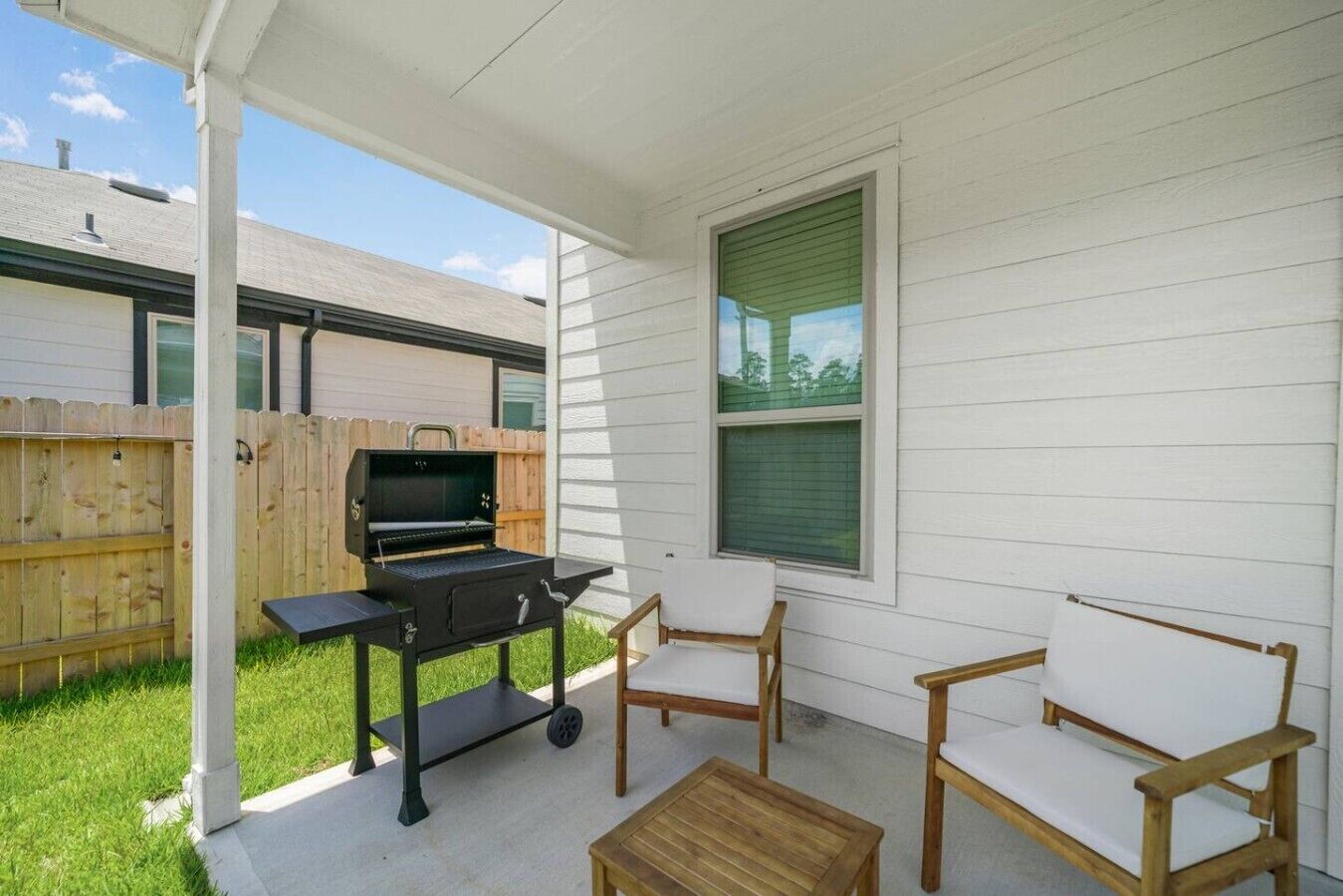 Eine überdachte Terrasse mit Grill, zwei Stühlen und einem kleinen Tisch.